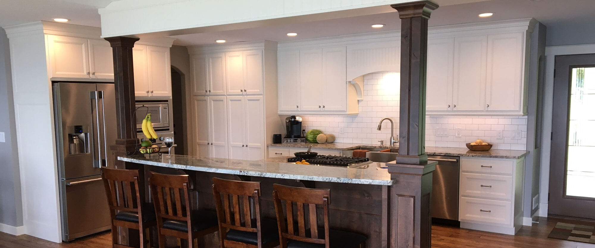 Custom kitchen cabinets made of solid wood and painted white featuring a breakfast bar island; designed, built, and installed by finewood Structures of Browerville, MN