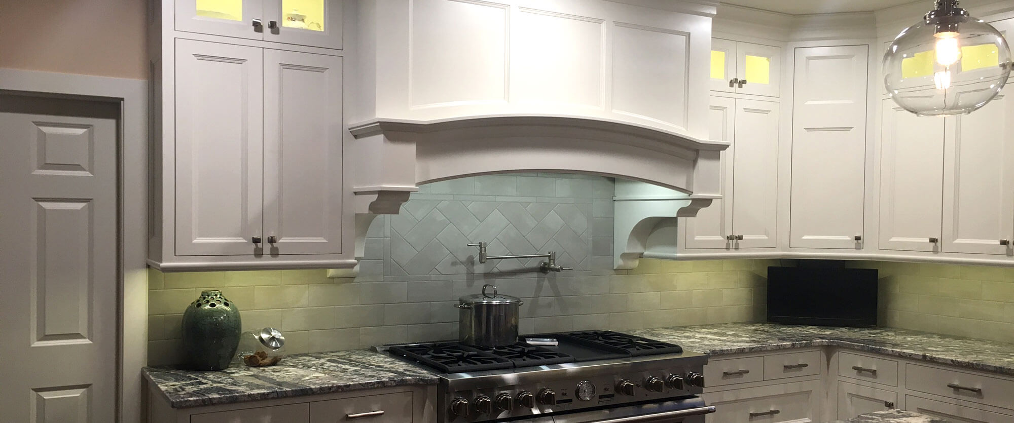 Custom kitchen cabinets made of solid wood and painted white featuring a curved range hood and lighted upper doors; designed, built, and installed by finewood Structures of Browerville, MN